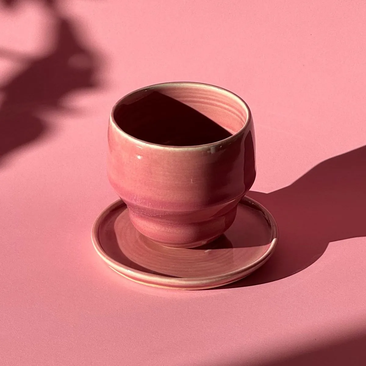 Pink cup with a curved foot on its saucer